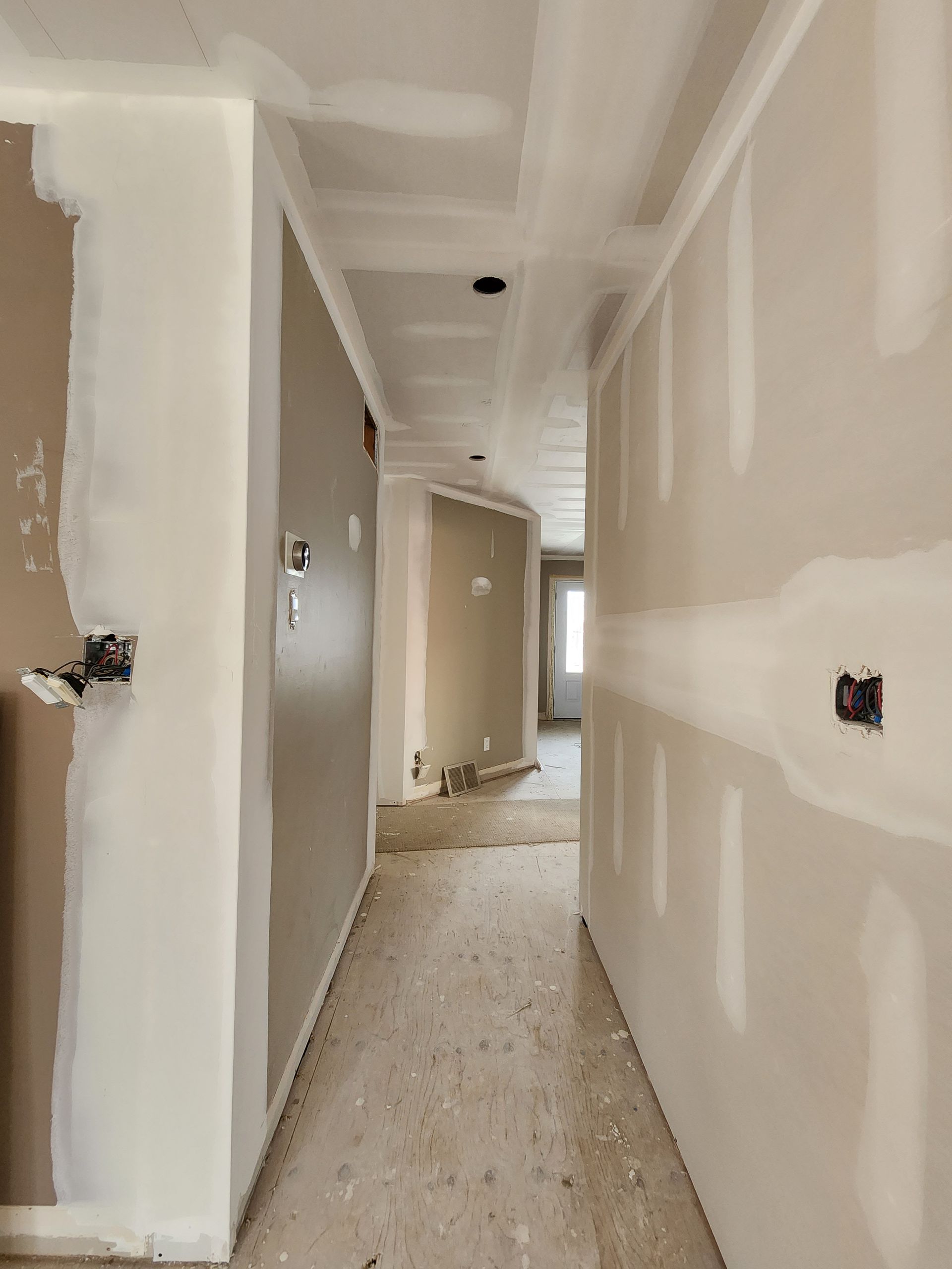 a long hallway in a house under construction with drywall on the walls .
