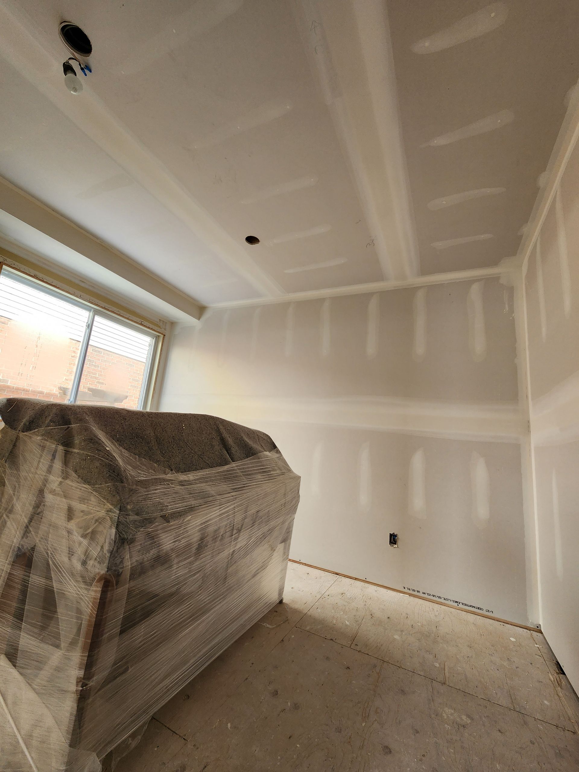 a room with drywall walls and a couch wrapped in plastic .