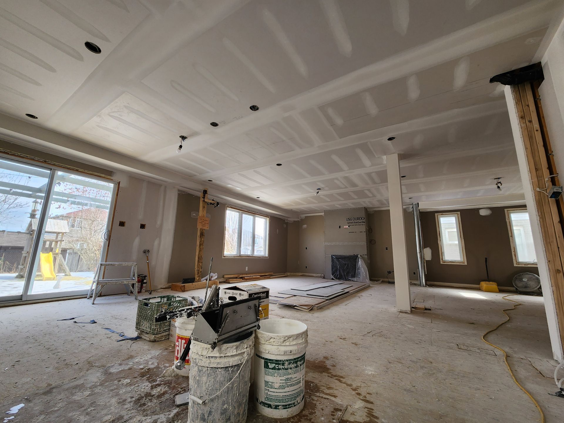 a large room under construction with buckets of paint on the floor .