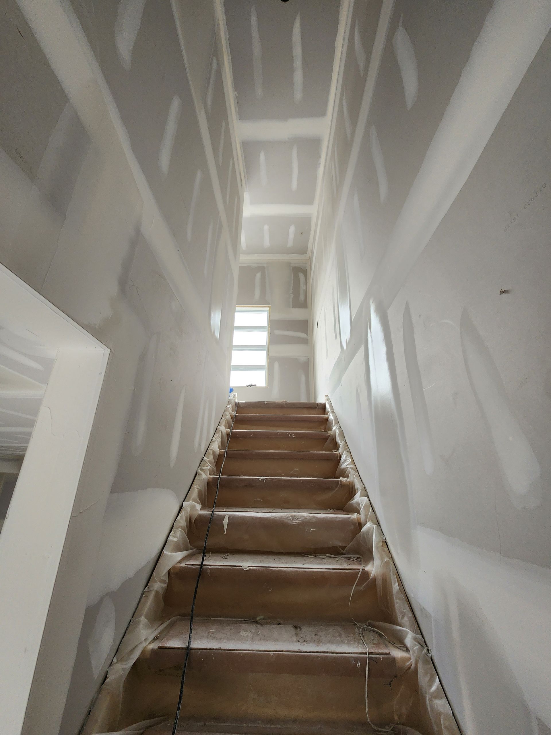 a staircase is going up a very long hallway with drywall walls .