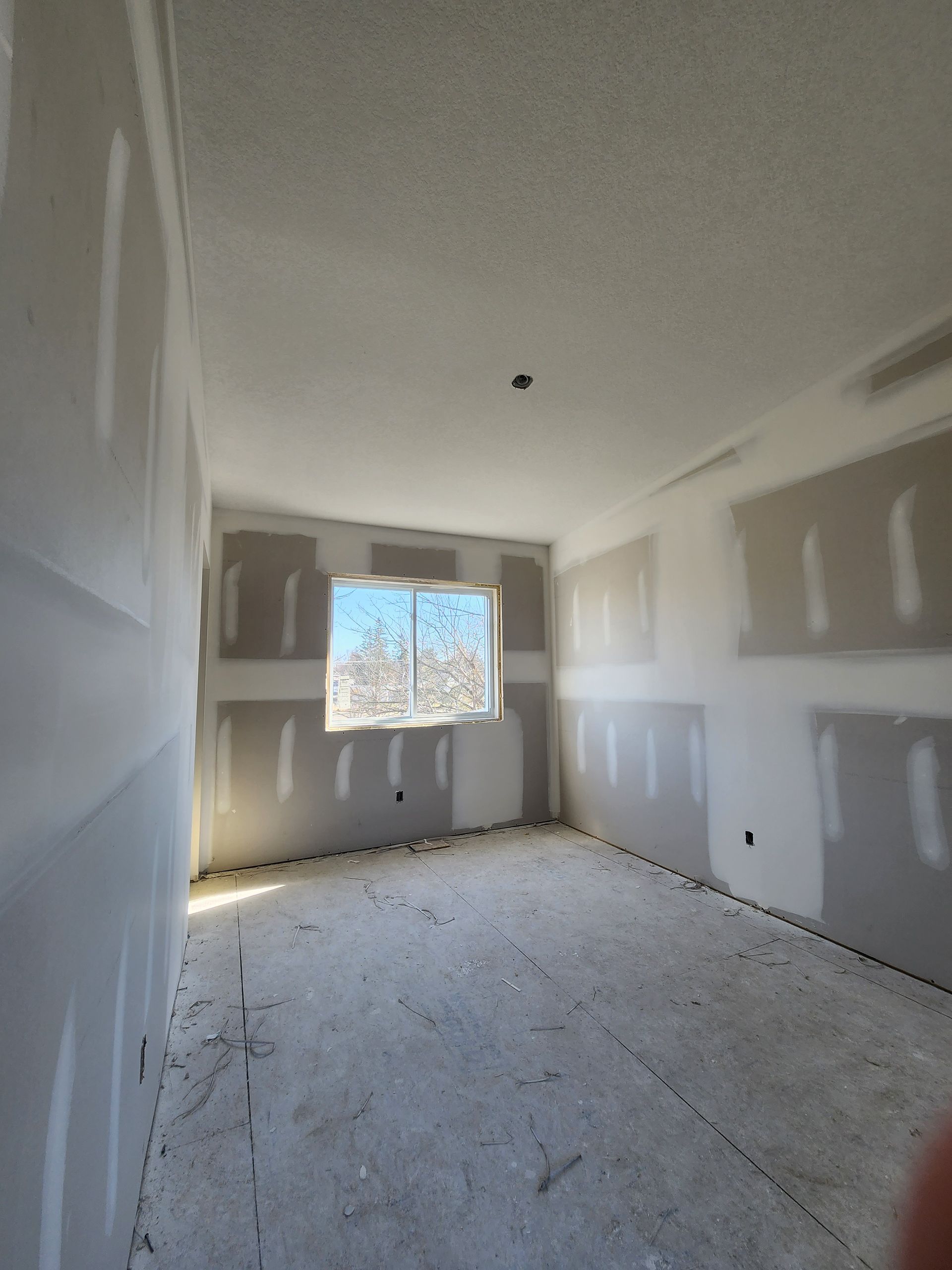 an empty room with drywall walls and a window .