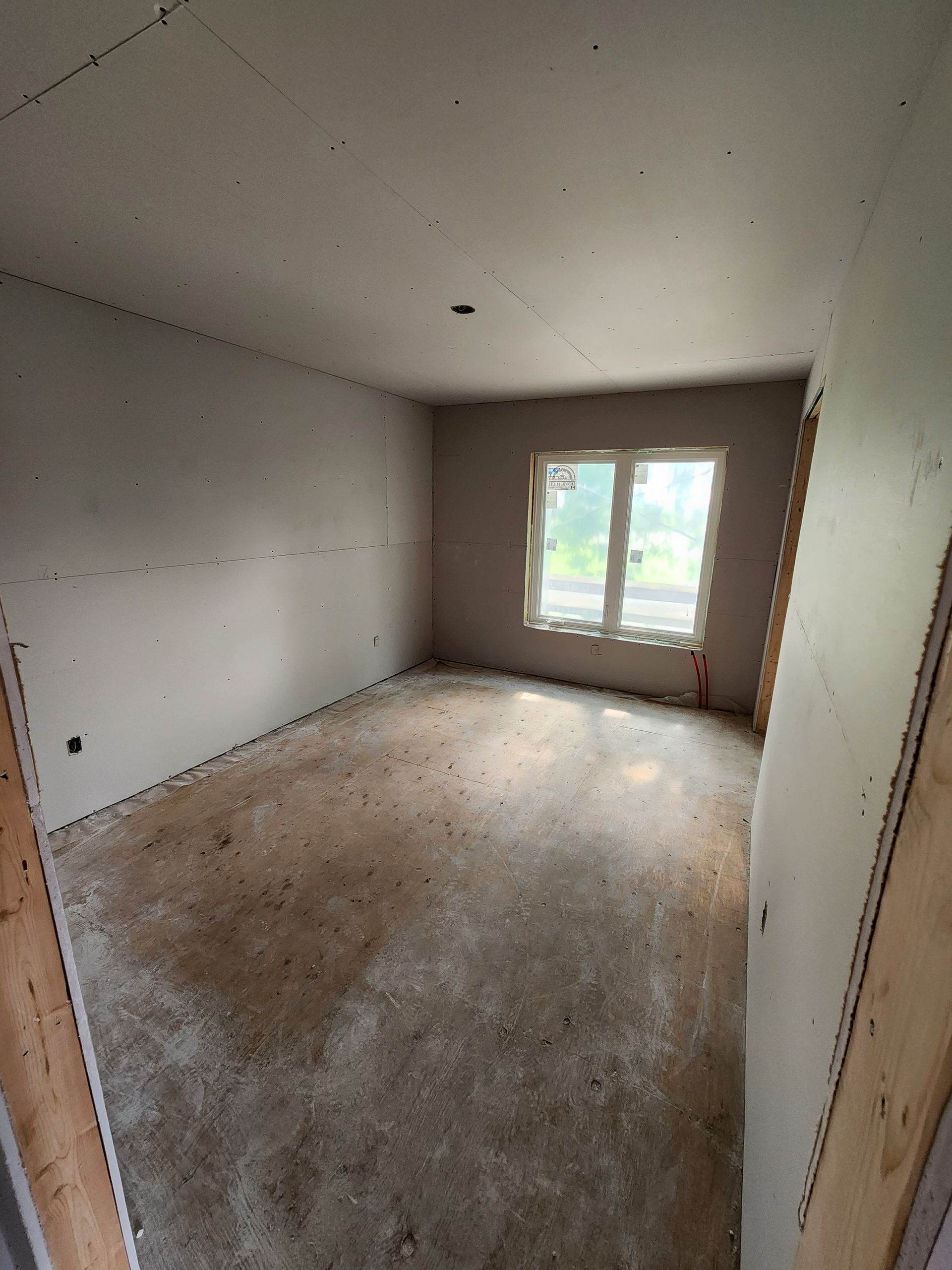 an empty room with a window and drywall on the walls .