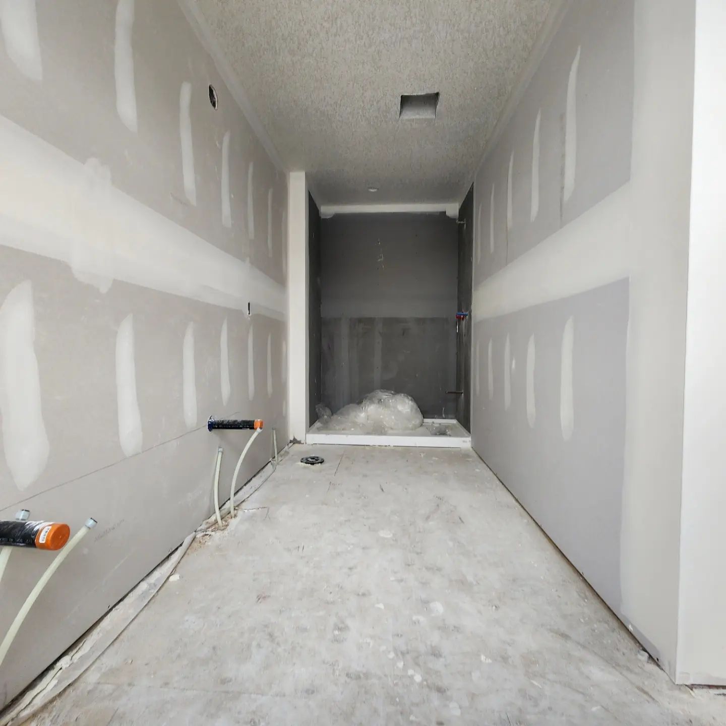 a long hallway with drywall walls and a concrete floor