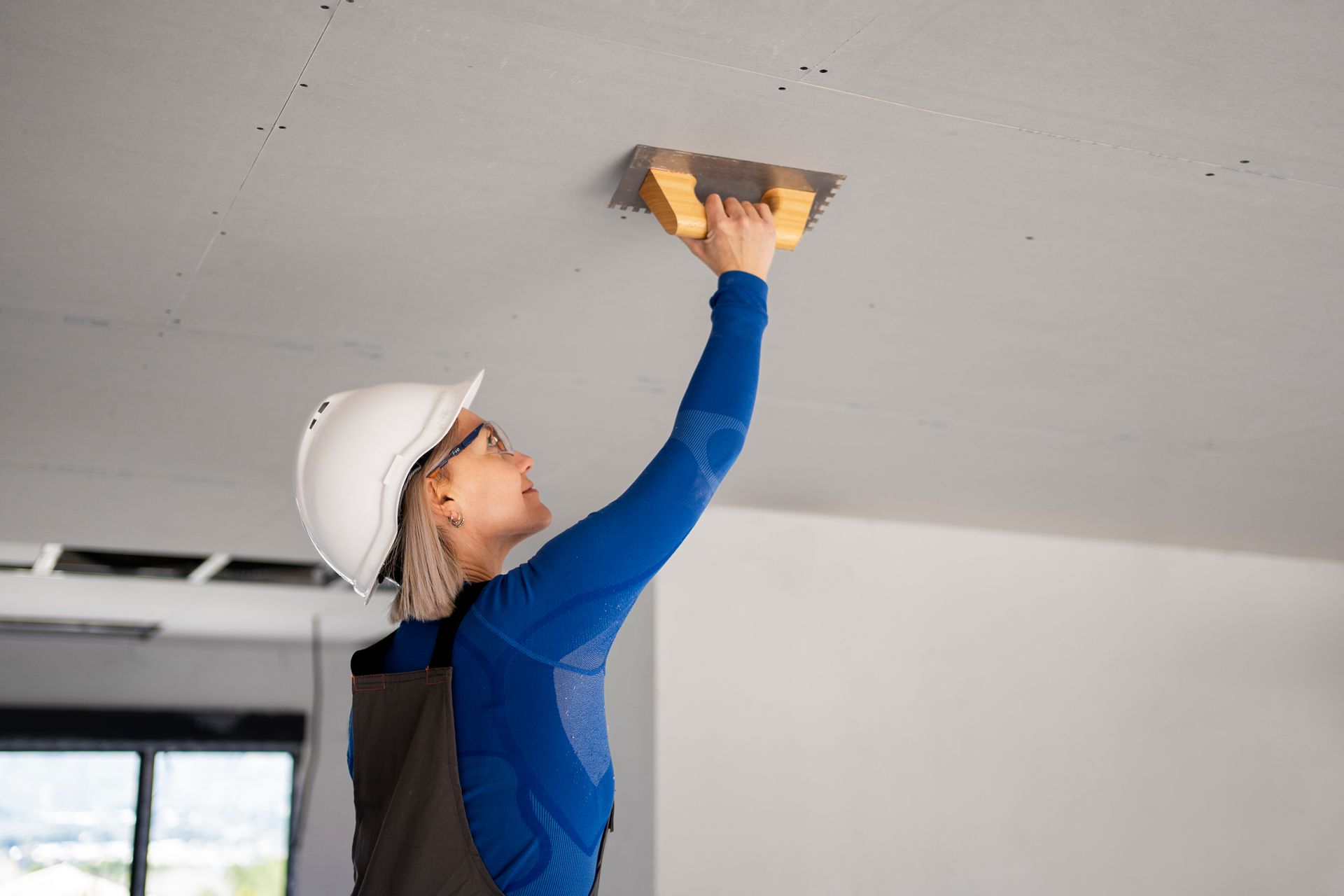 A woman in a hard hat is working on a ceiling.