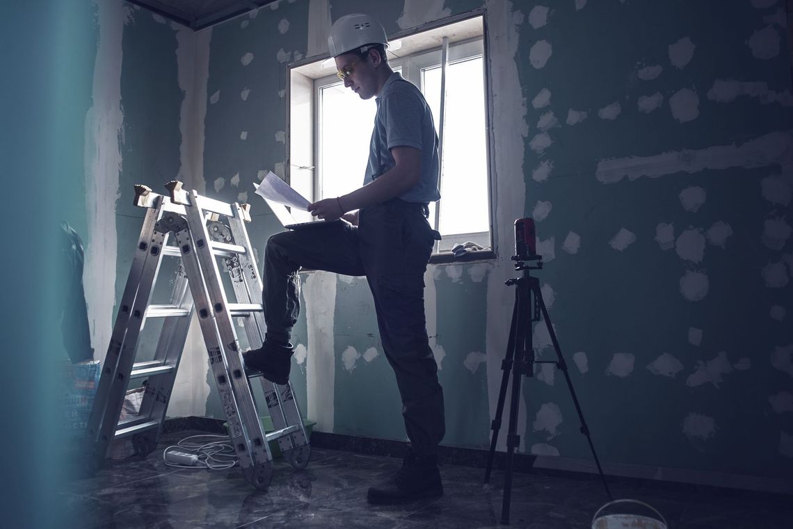 a man is standing on a ladder in a room looking at a piece of paper .