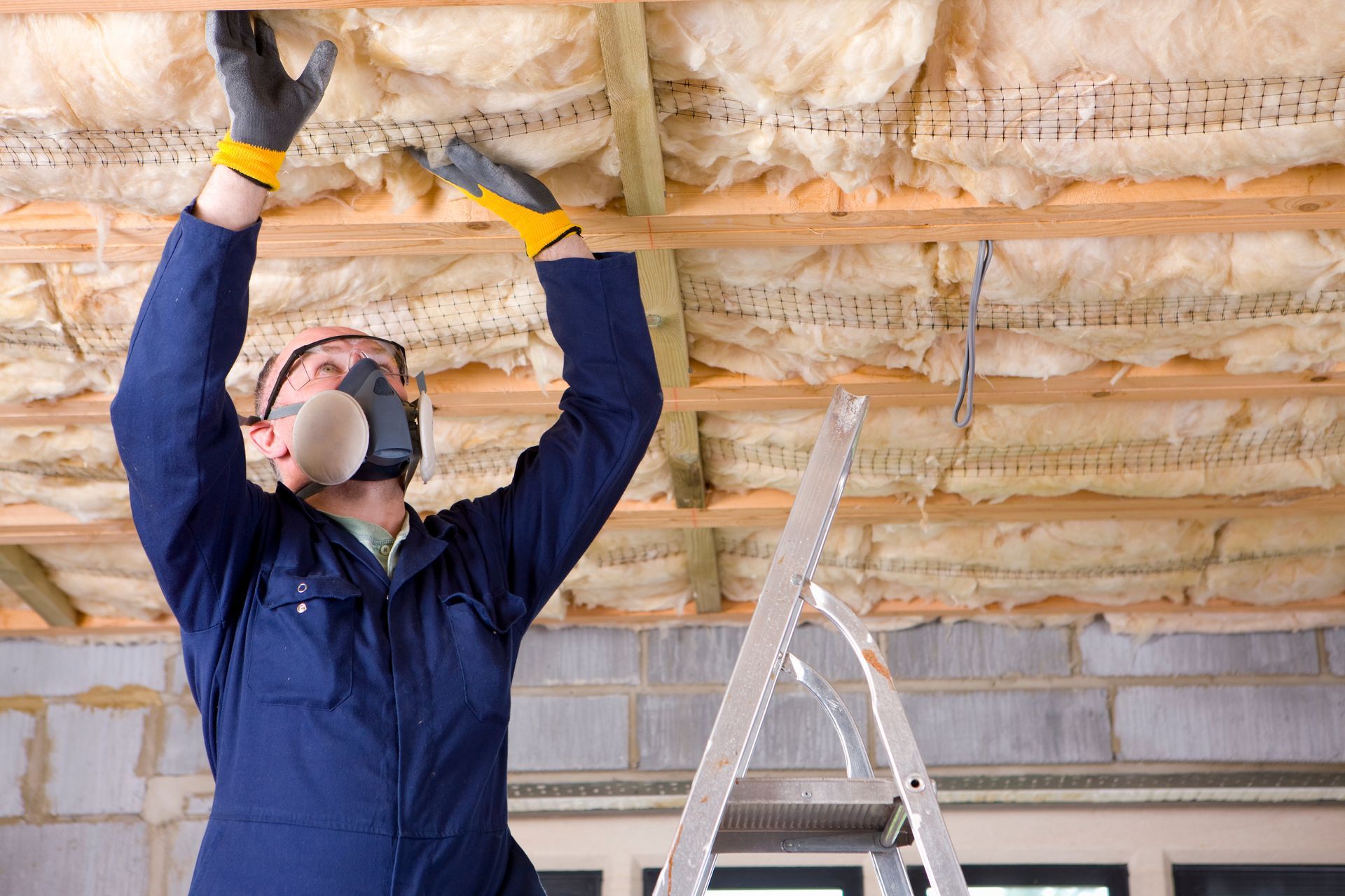 A man wearing a mask and gloves is working on a ceiling.