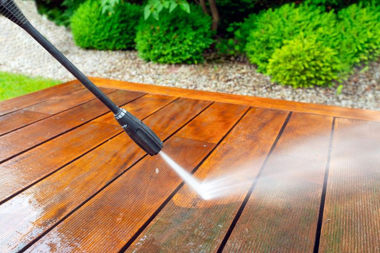 A person is using a high pressure washer to clean a wooden deck.
