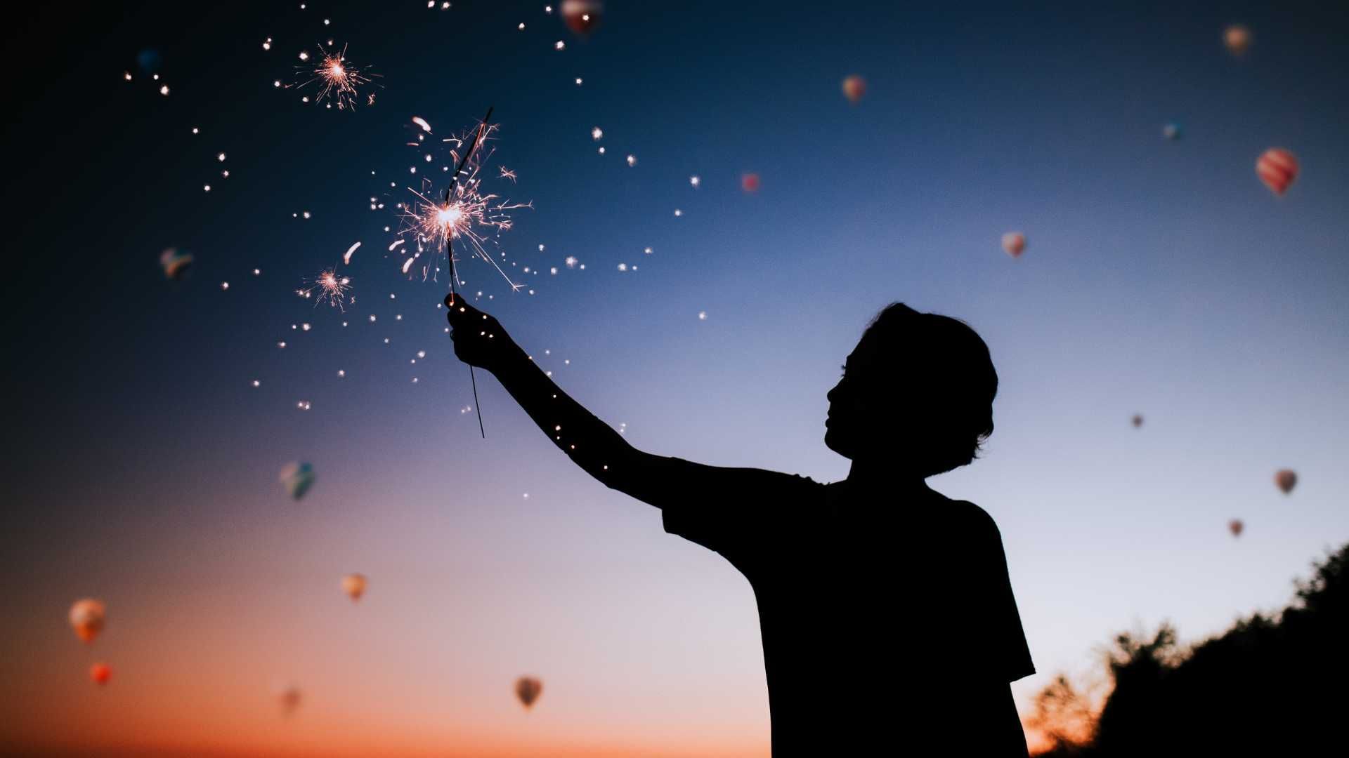 A silhouette of a person holding a sparkler in the air.