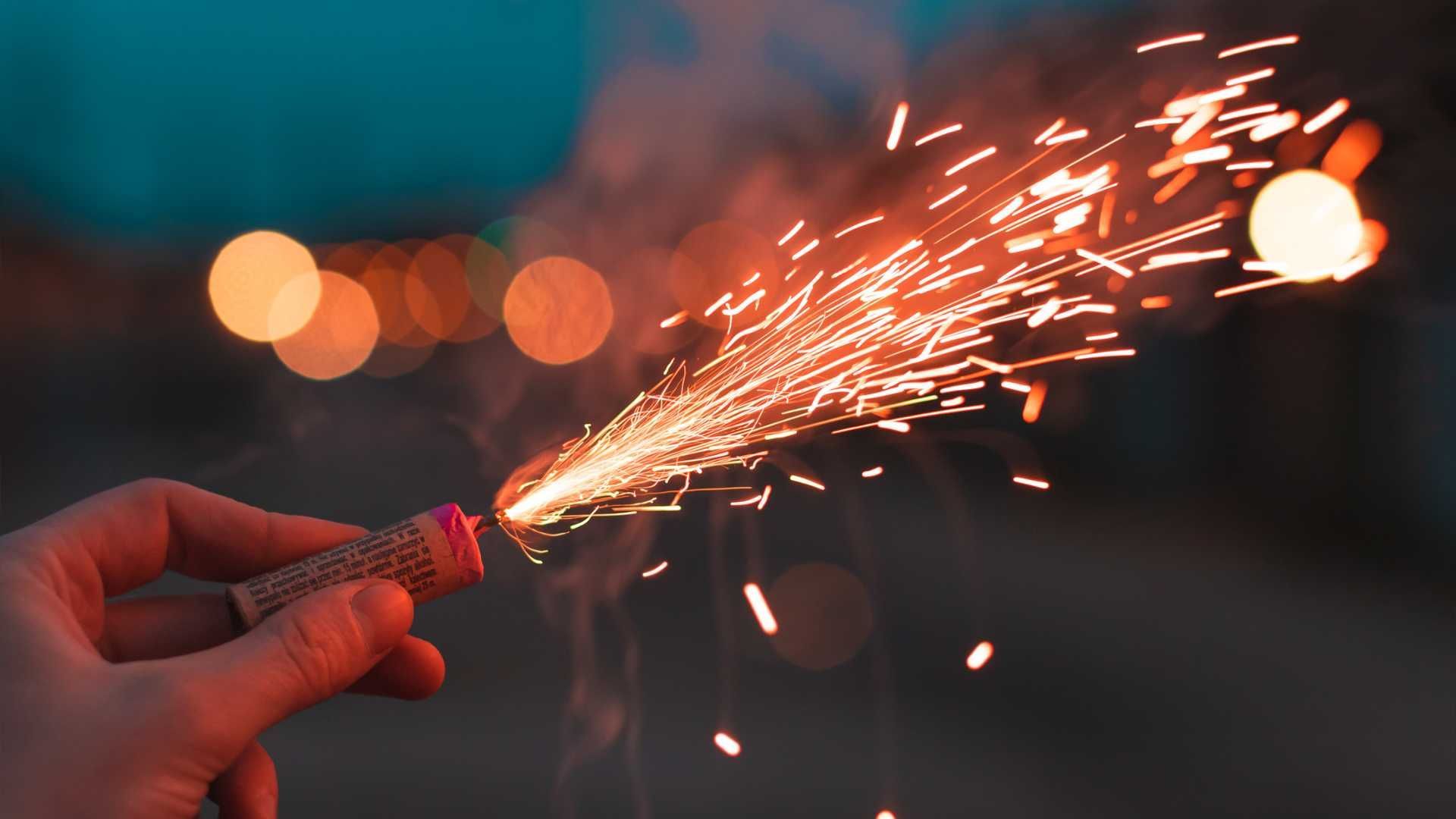 A person is holding a firework in their hand with sparks coming out of it.
