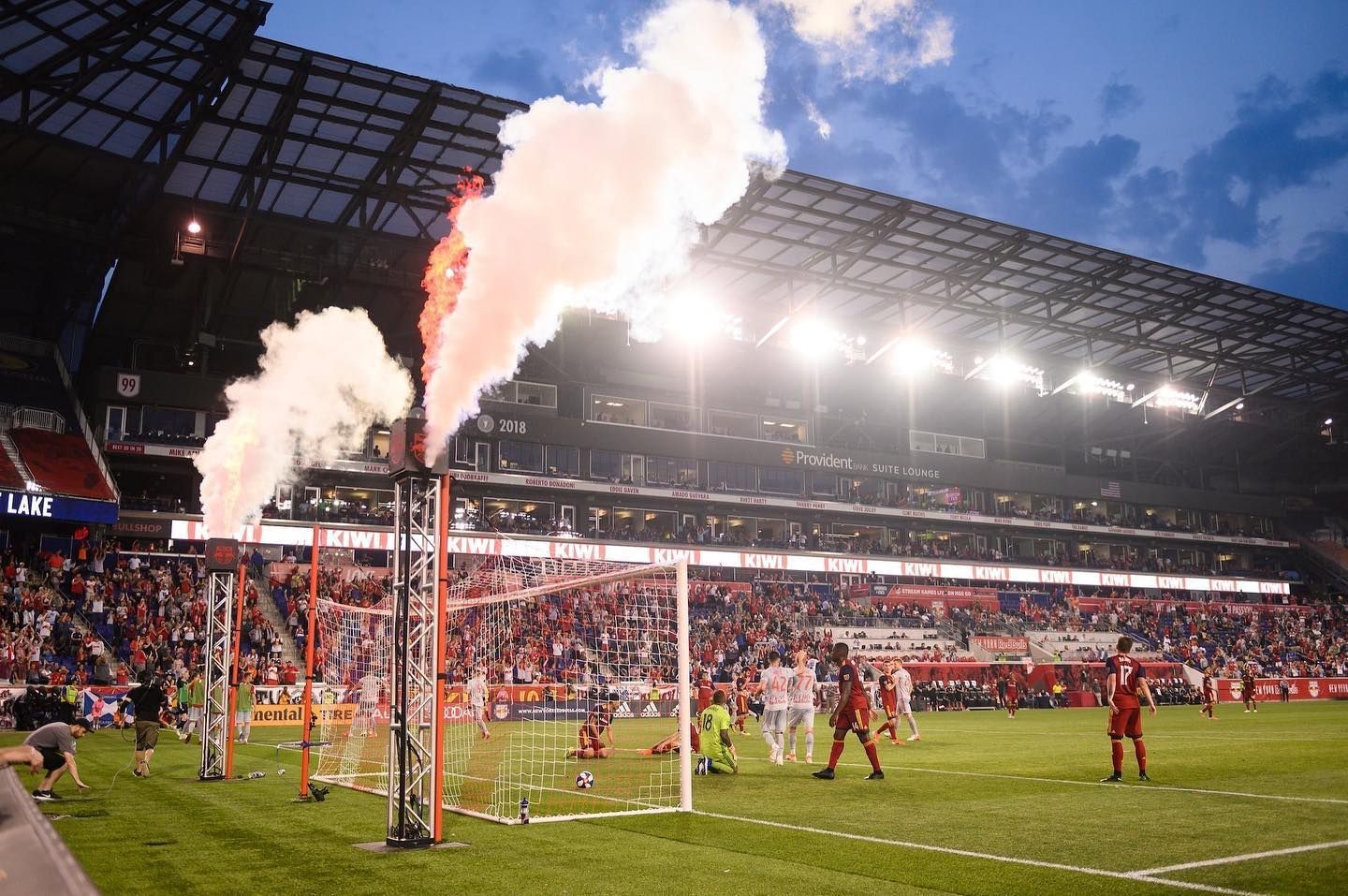 A soccer game is being played in a stadium with smoke coming out of the stands.