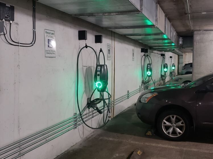 A row of electric vehicle charging stations mounted on a concrete wall in a parking garage, with green lights illuminated.