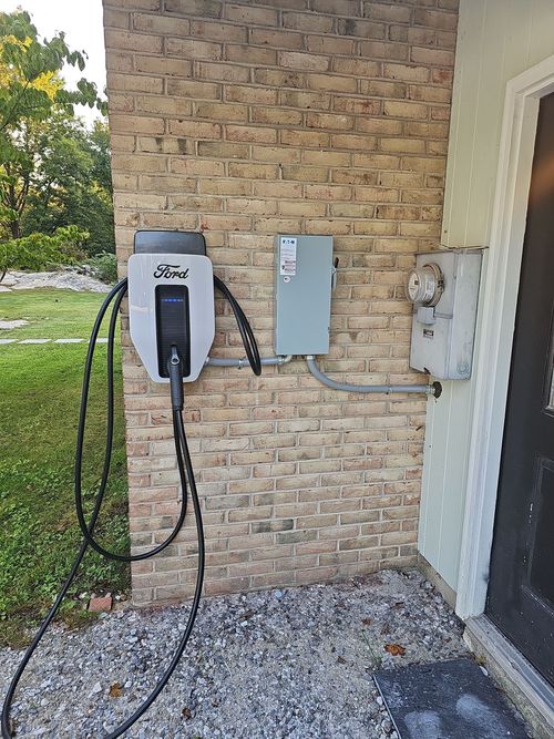 An electric vehicle charging station mounted on a brick exterior wall next to an electrical meter box.