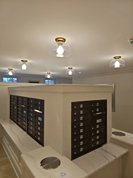 A central island in a room features rows of black wall-mounted mailboxes set into a cream-colored, marble-topped structure.