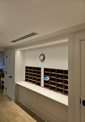 A wooden mail cubby unit with an integrated white counter and overhead lighting set against a wall with a wall clock.