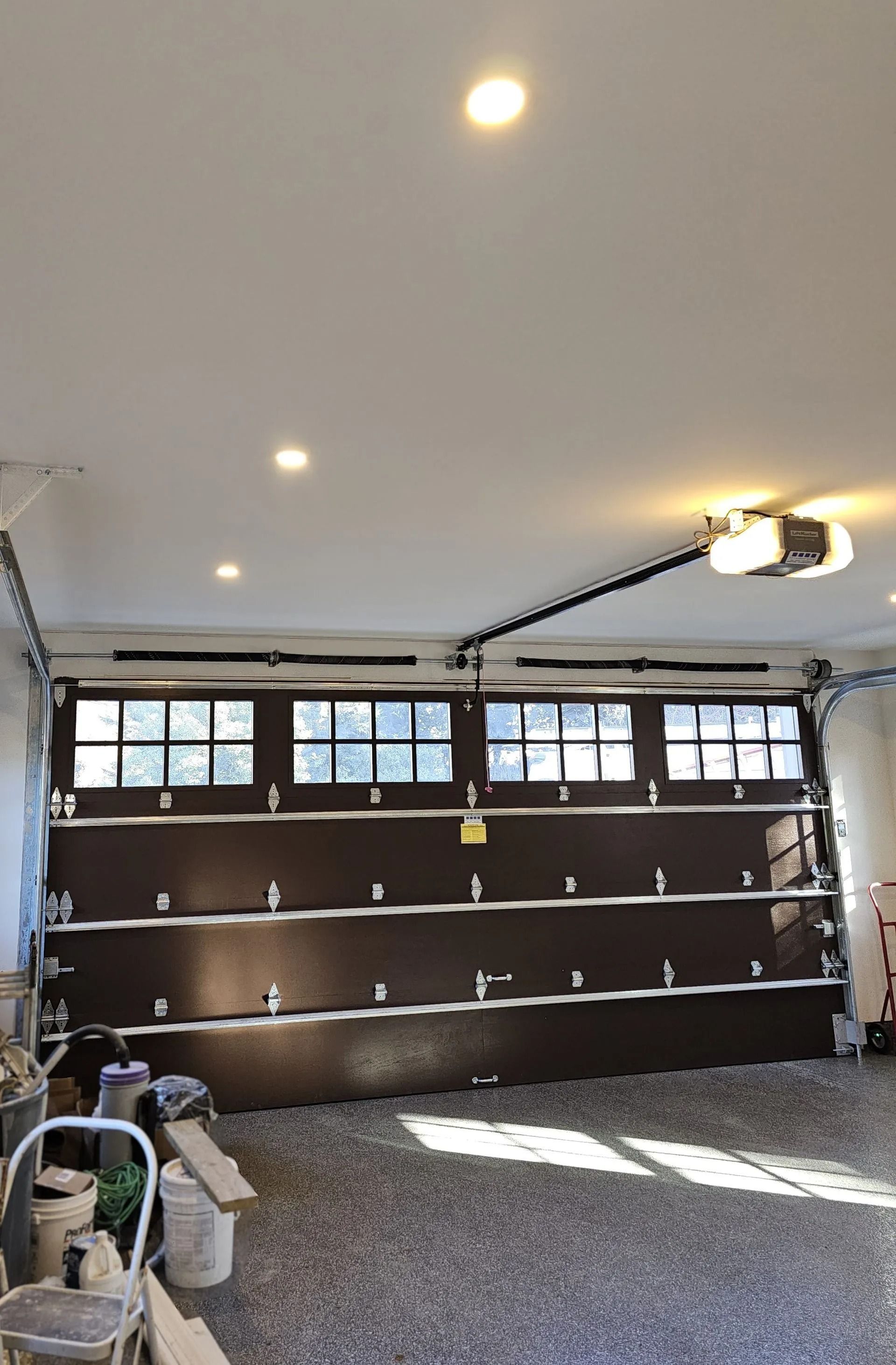 A dark brown residential garage door with rectangular windows, viewed from inside a garage with a concrete floor.