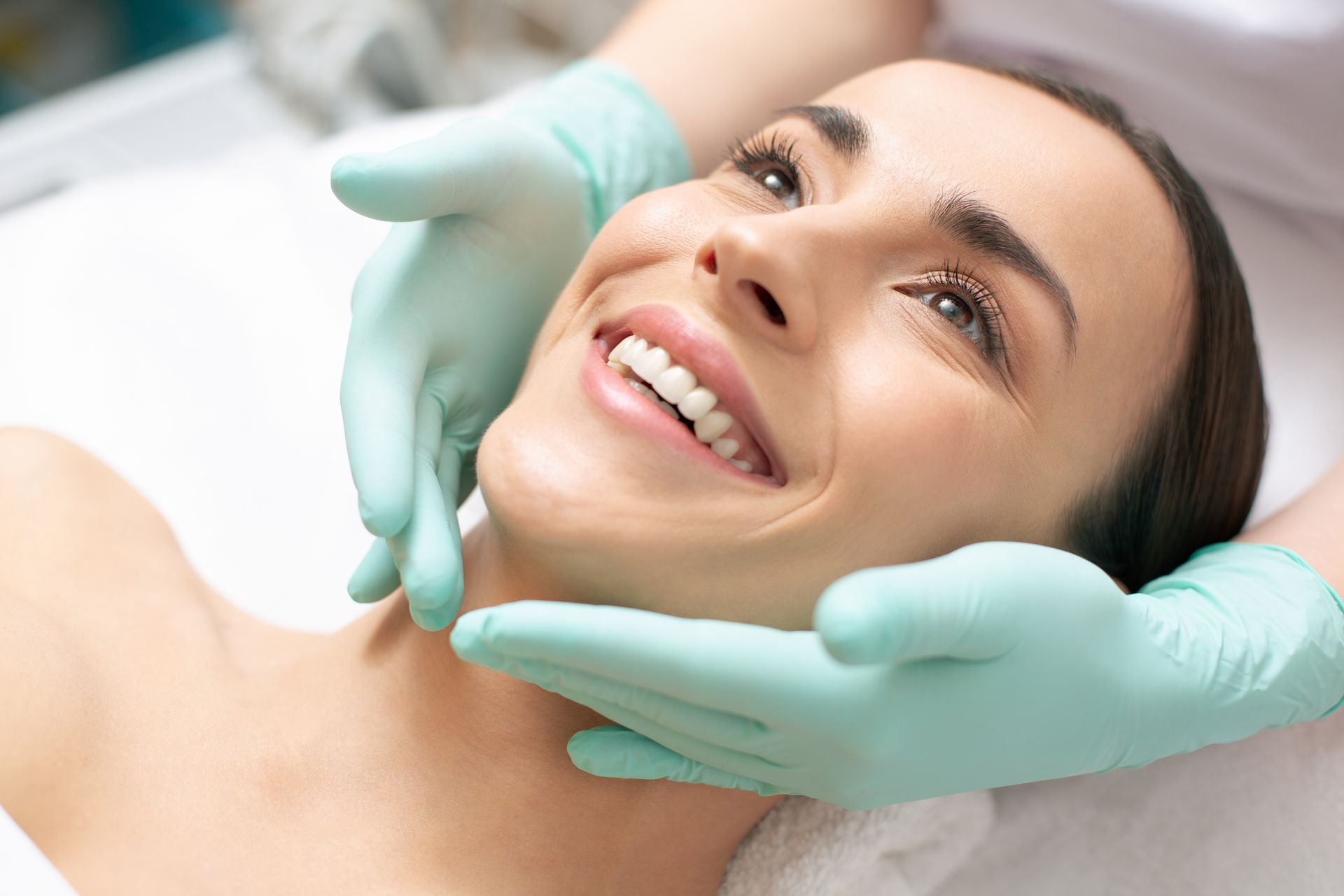 Close-up of a smiling woman and hands in green rubber gloves touching it gently at a medical spa.