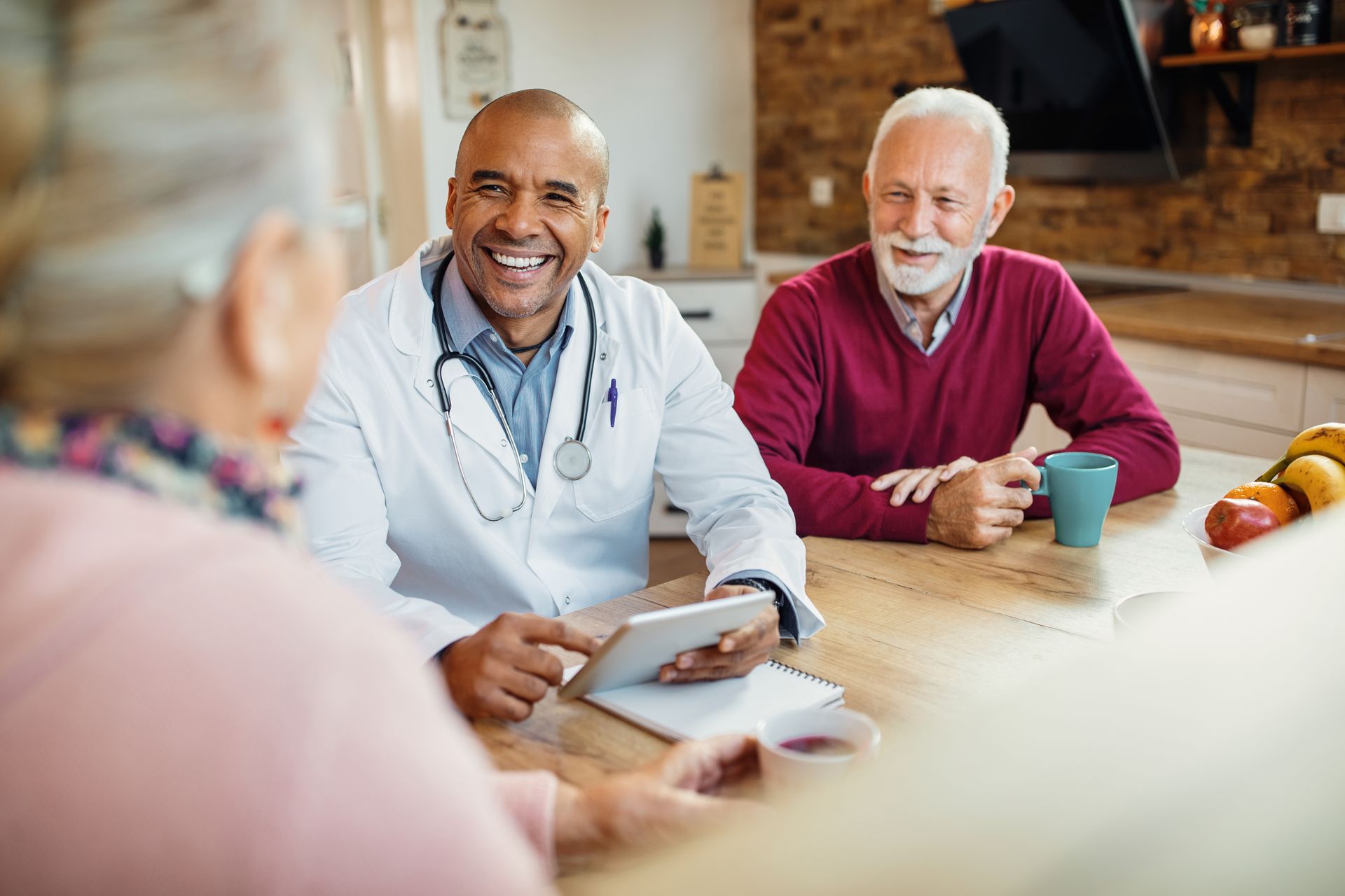 A doctor is sitting at a table talking to two elderly people.