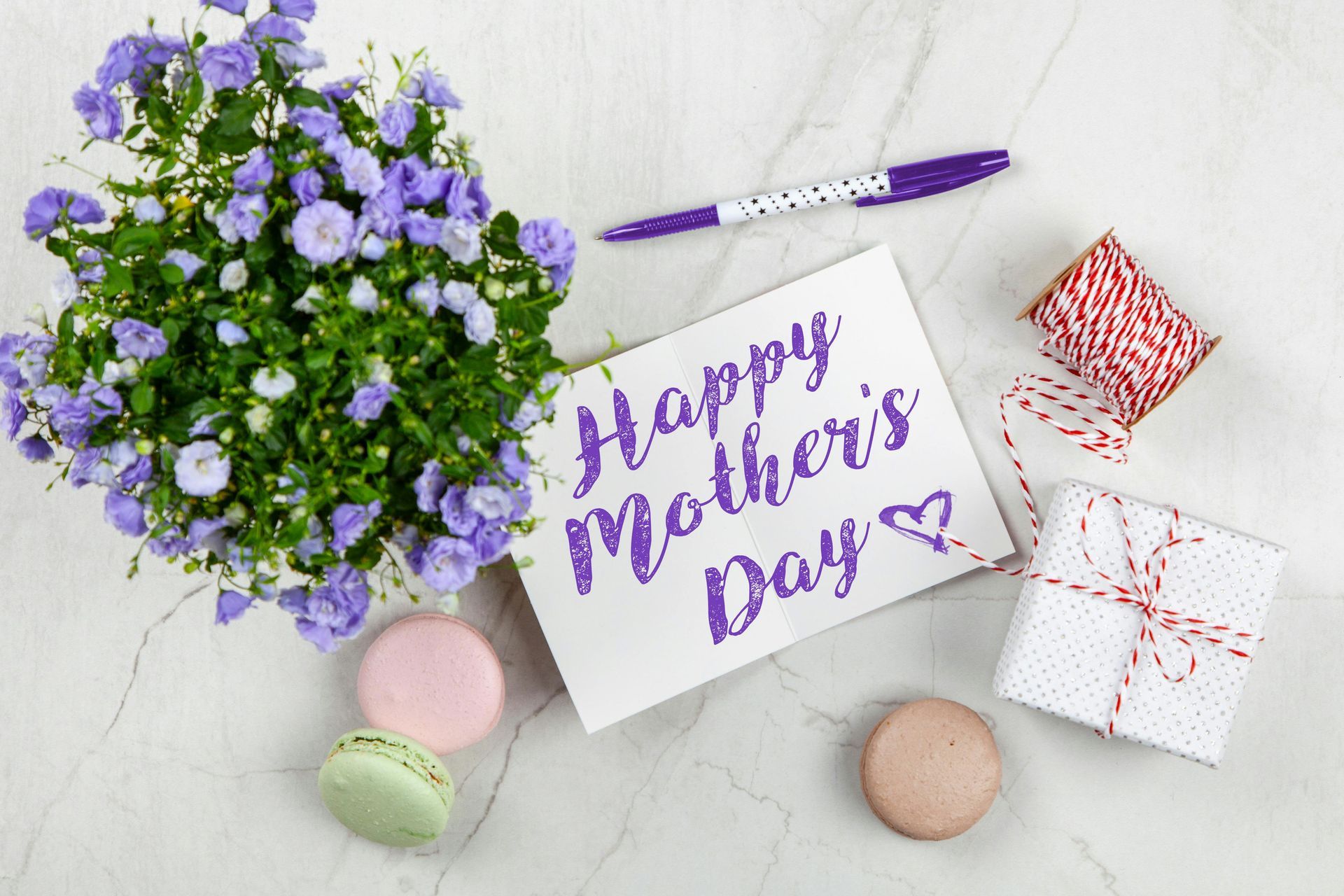 A happy mother 's day card with flowers , macarons , gifts and a pen.