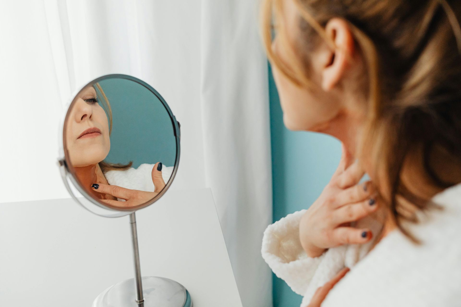 A woman is looking at her neck in a mirror.