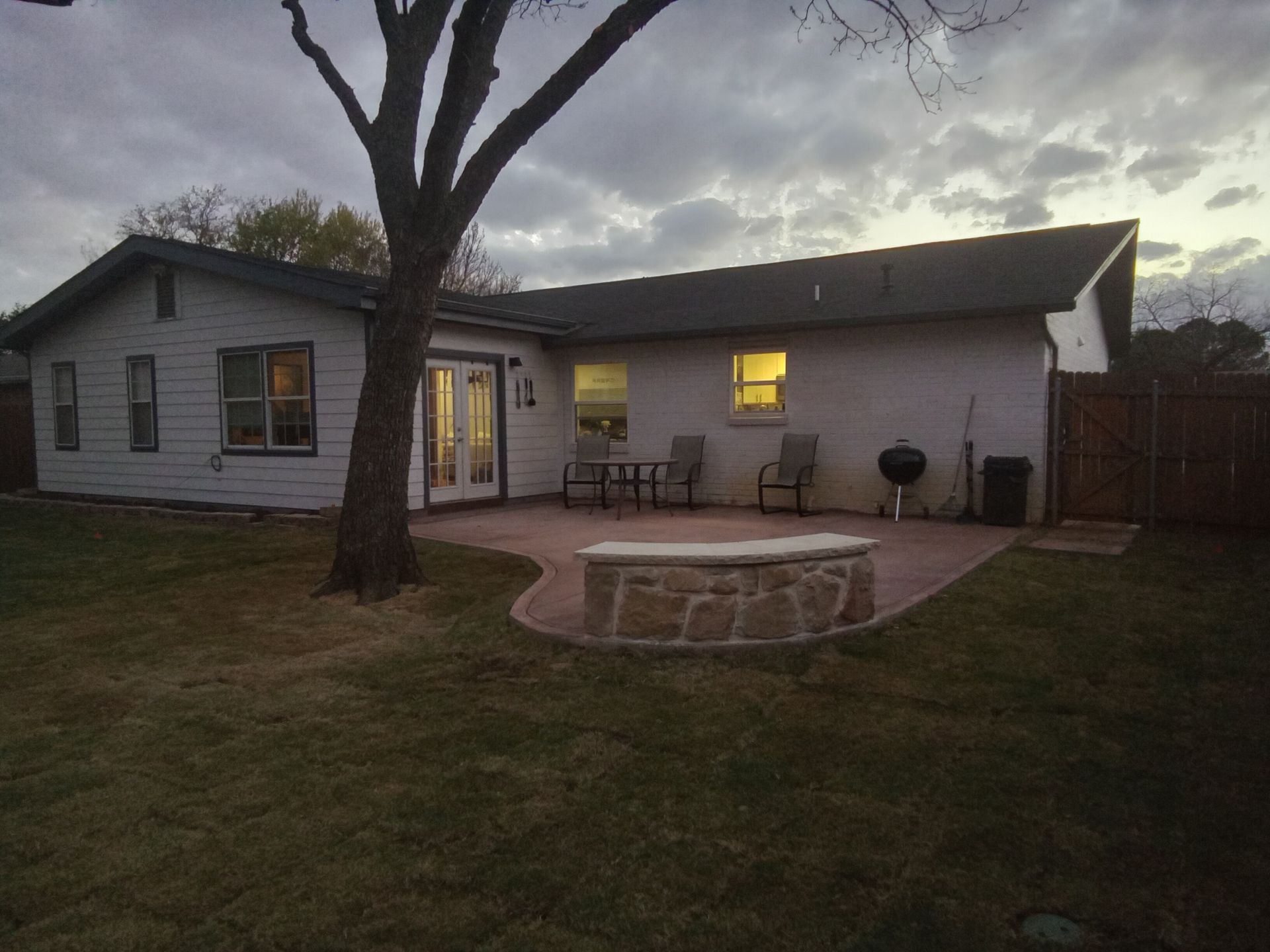 Backyard patio with seating, a fire pit, and a grill, viewed at dusk.