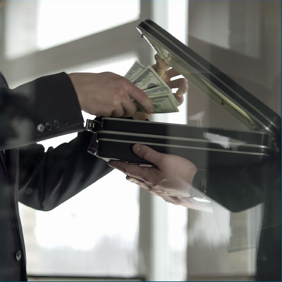 A person in a dark suit places a stack of US dollar bills into an open briefcase held by another person.