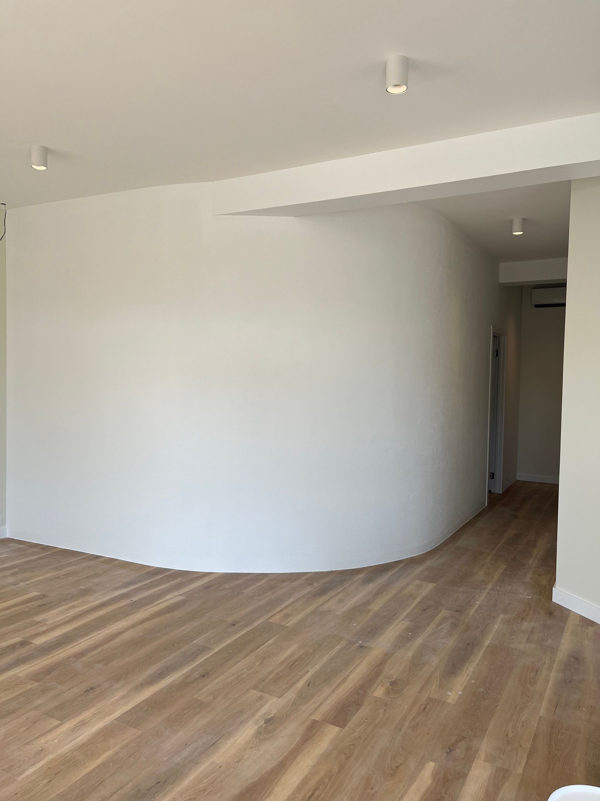 A minimalist room with light wood floors, a large curved white feature wall, and recessed ceiling lighting — GV painting in Shepparton, VIC