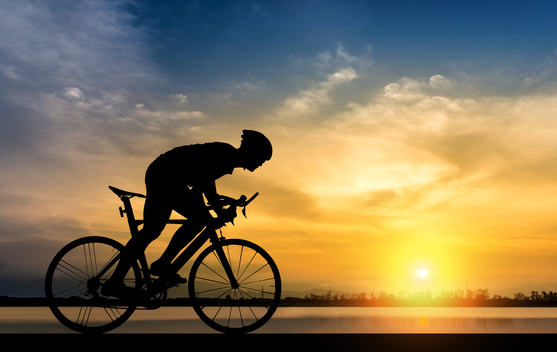 A silhouette of a person riding a bike at sunset.