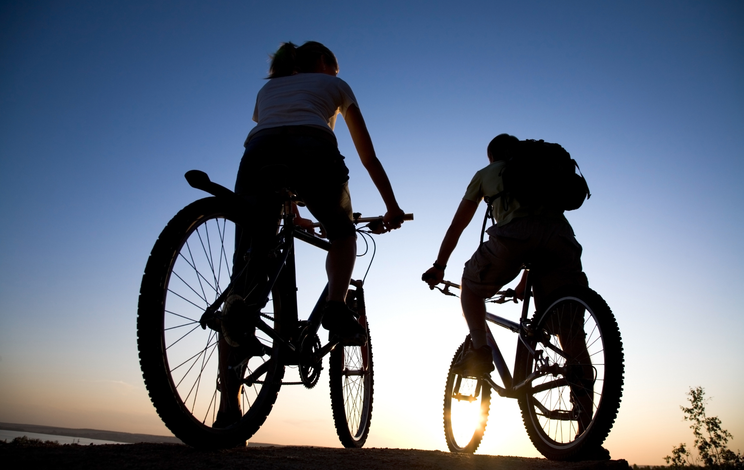 A man and a woman are riding bicycles at sunset