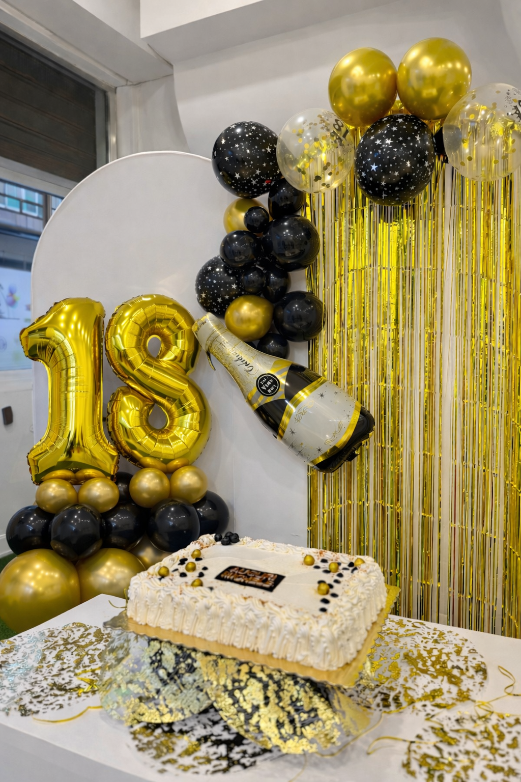 Donna con torta per il suo 18° compleanno, sorridente circondata da persone che applaudono, in un interno con palloncini.