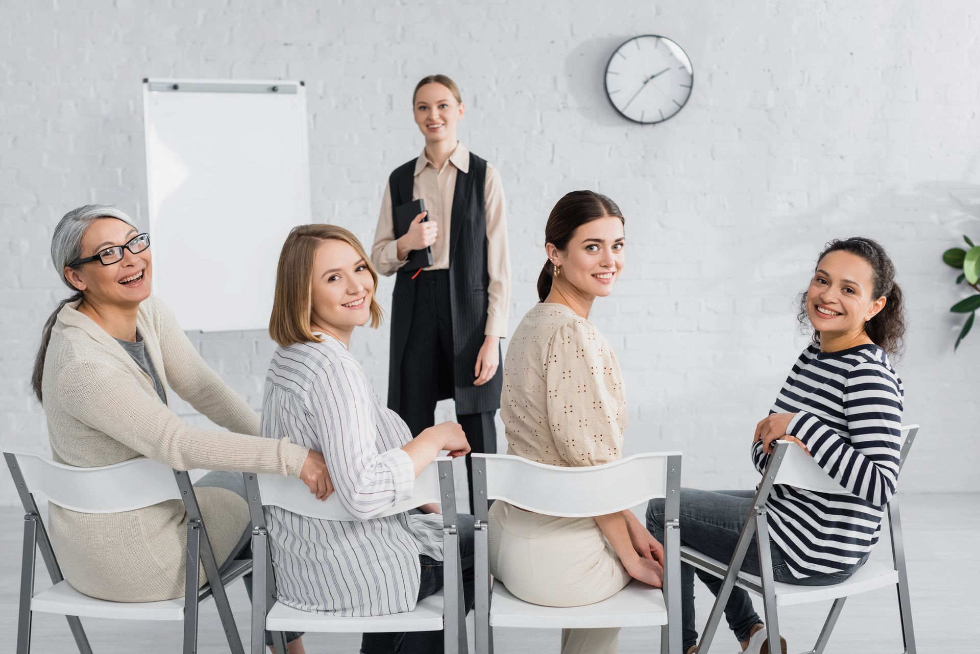 Cinque donne in una stanza luminosa, sedute e in piedi vicino a una lavagna. La donna in piedi sorride.