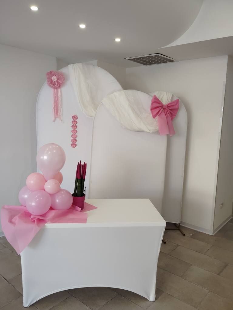 Sfondo per il ricevimento di nozze con decorazioni rosa e bianche: palloncini, tessuto e un tavolo.