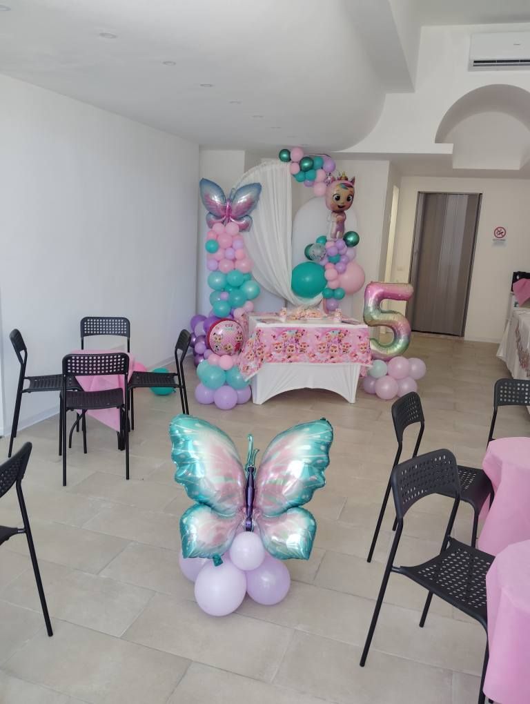 Decorazioni per feste di compleanno a tema farfalle e palloncini; palloncini rosa, blu e bianchi, tavolo e sedie.