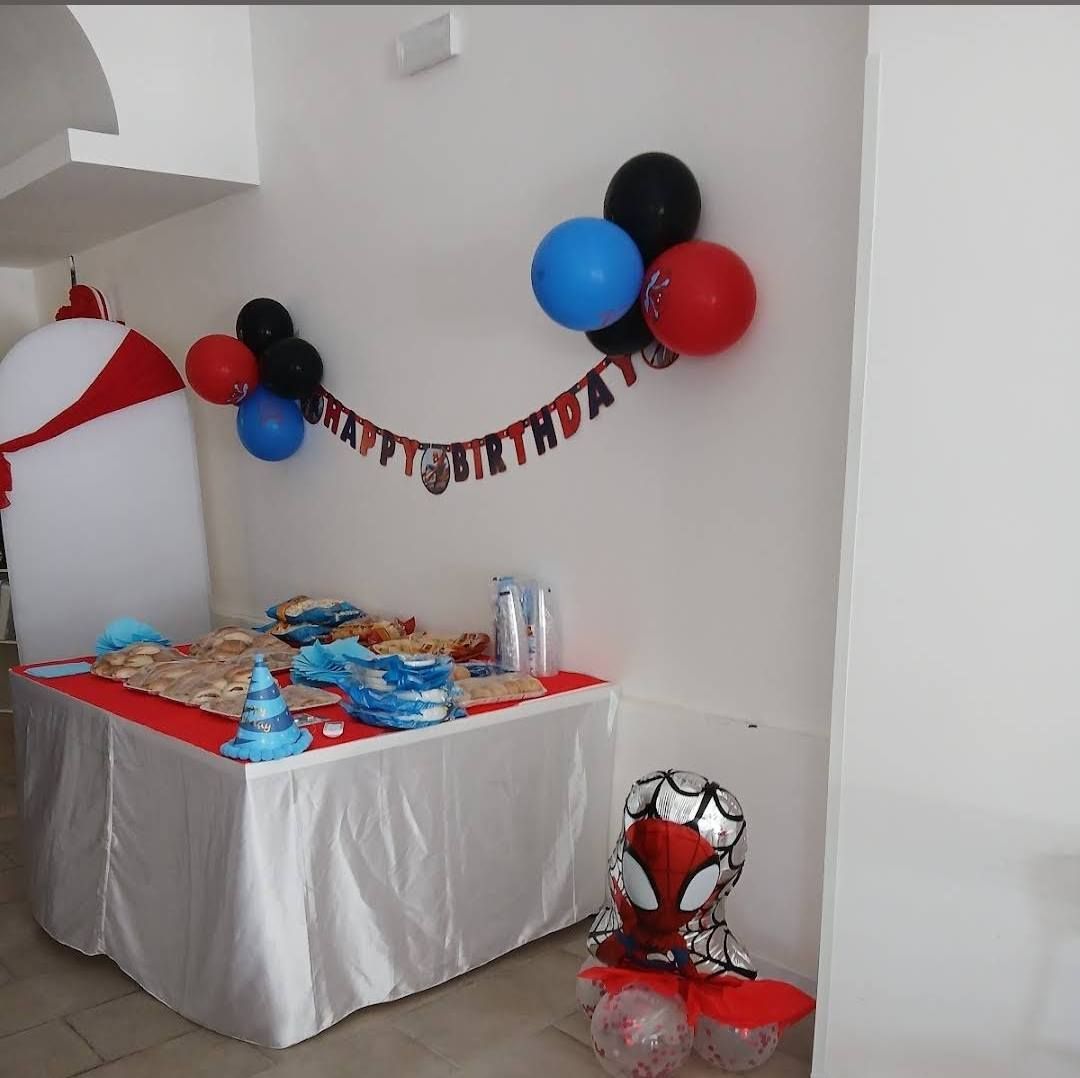 Allestimento per festa di compleanno a tema Spiderman, con palloncini, tavolo con cibo e decorazioni.