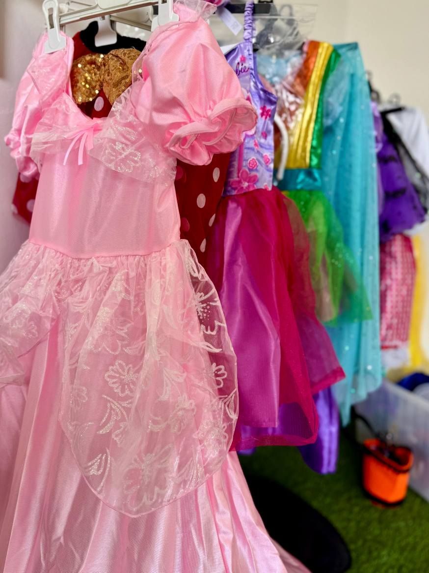 Un vestito rosa da principessa e altri costumi colorati appesi a un attaccapanni.