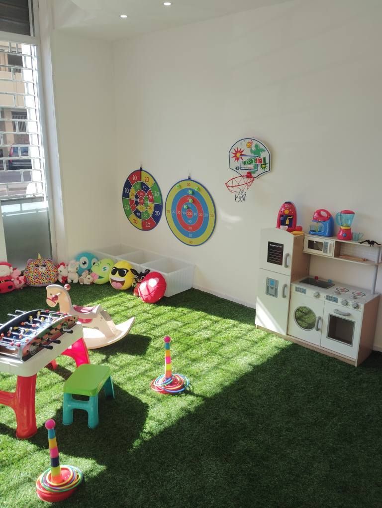 Sala giochi con erba artificiale, giocattoli e giochi come calcio balilla, freccette e una cucina giocattolo.