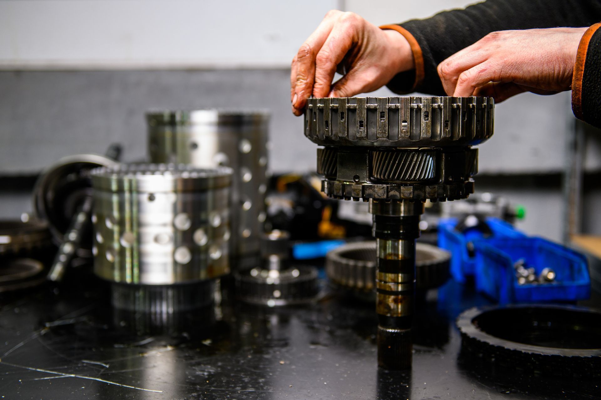 Auto transmission rebuild with mechanic working on disassembled gearbox parts on metal table.