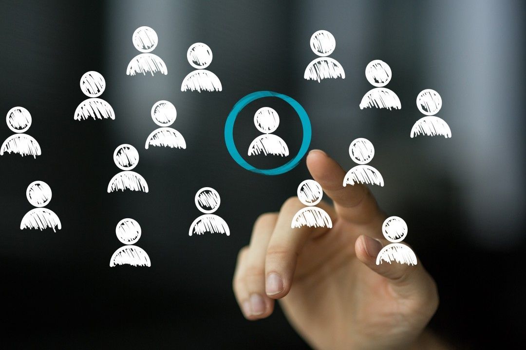 A hand is pointing at a person in a circle surrounded by other people.