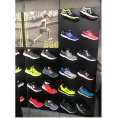 Sneakers New Balance esposte in un negozio. Sfondo con grafica di corridori. Vari colori e modelli su scaffali neri.