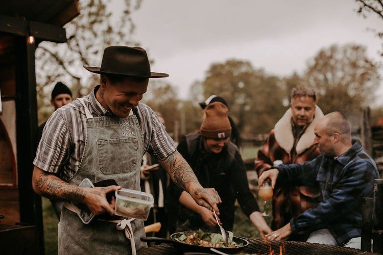 A man is cooking food in a pan in front of a group of people.