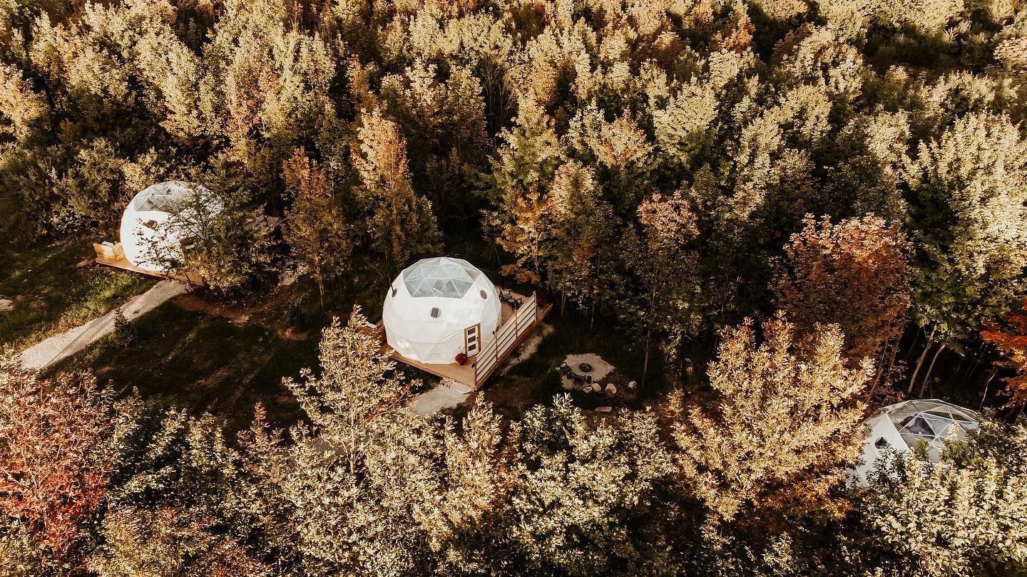 An aerial view of three dome tents in the middle of a forest.