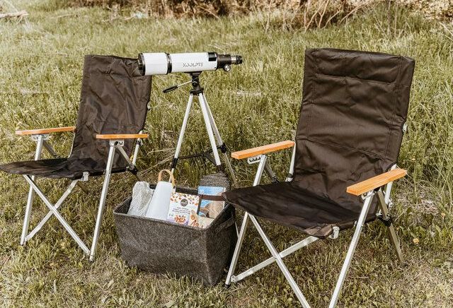 Two folding chairs and a telescope are sitting in the grass.