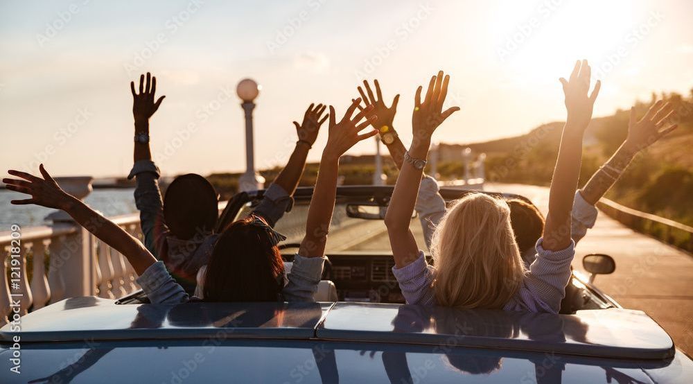 A group of people are sitting in a car with their arms in the air.