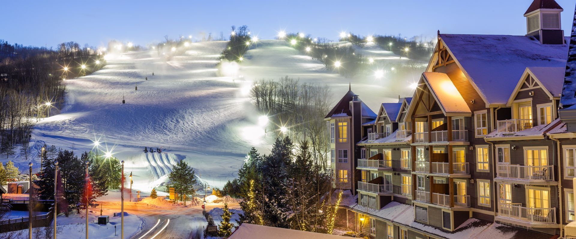 A ski resort at night with a large building in the foreground and a ski slope in the background.