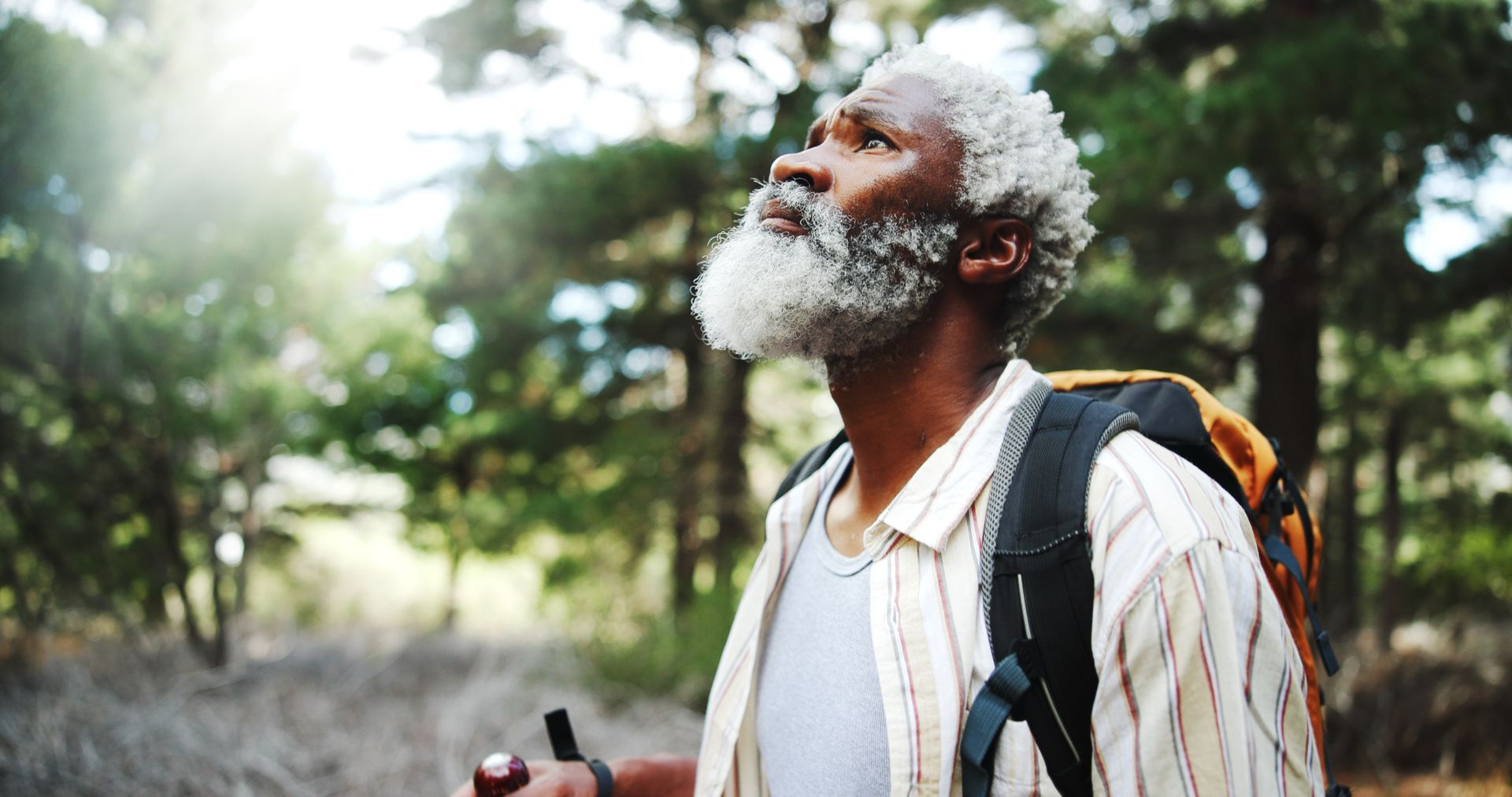 A man with a beard and a backpack is hiking in the woods.