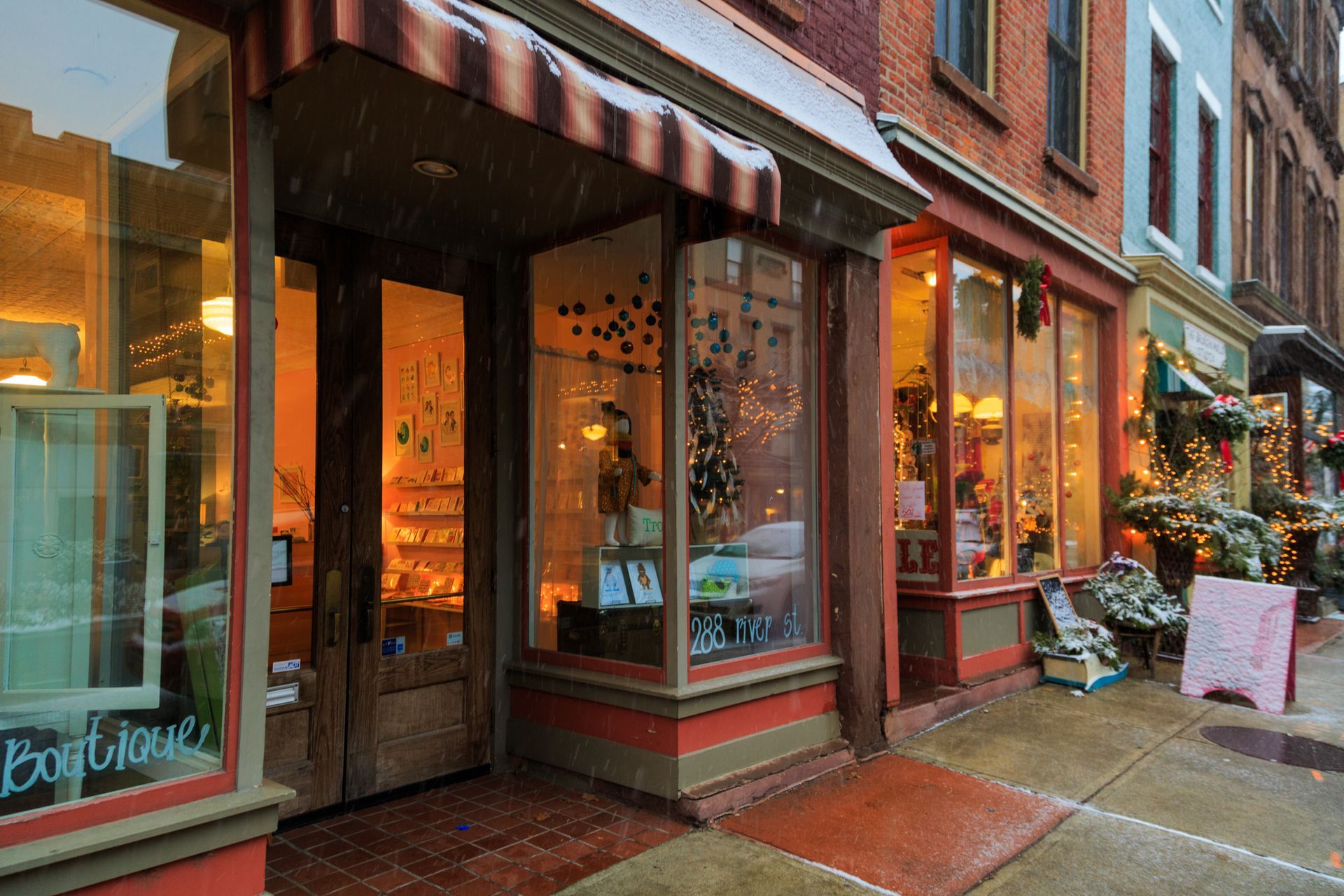 Shops along a street; snowy weather. Display windows with merchandise, orange and brown awnings.