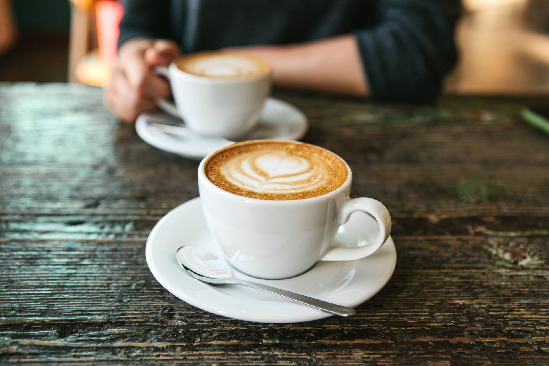 Two cappuccinos on white saucers on a rustic wooden table; one with latte art.