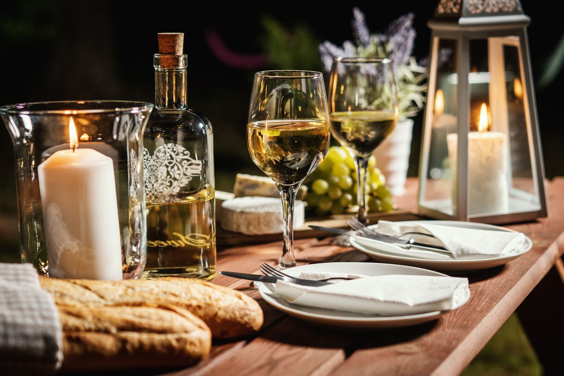 A wooden table topped with plates , candles , wine glasses and bread.