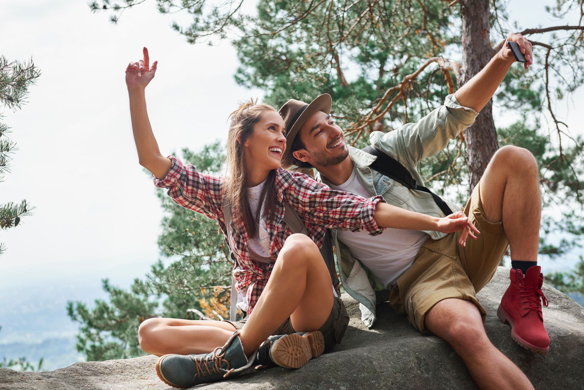 A man and a woman are sitting on a rock taking a selfie.