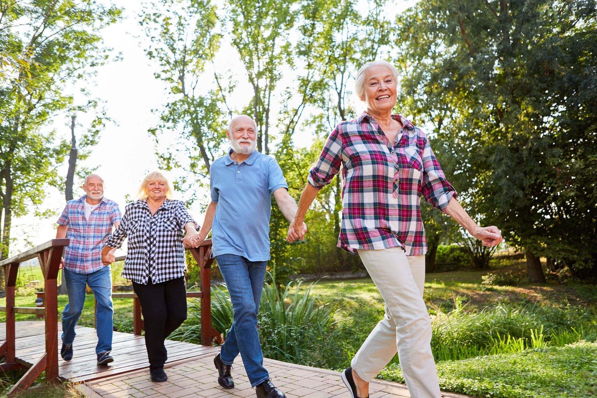 A group of elderly people are walking across a wooden bridge holding hands.