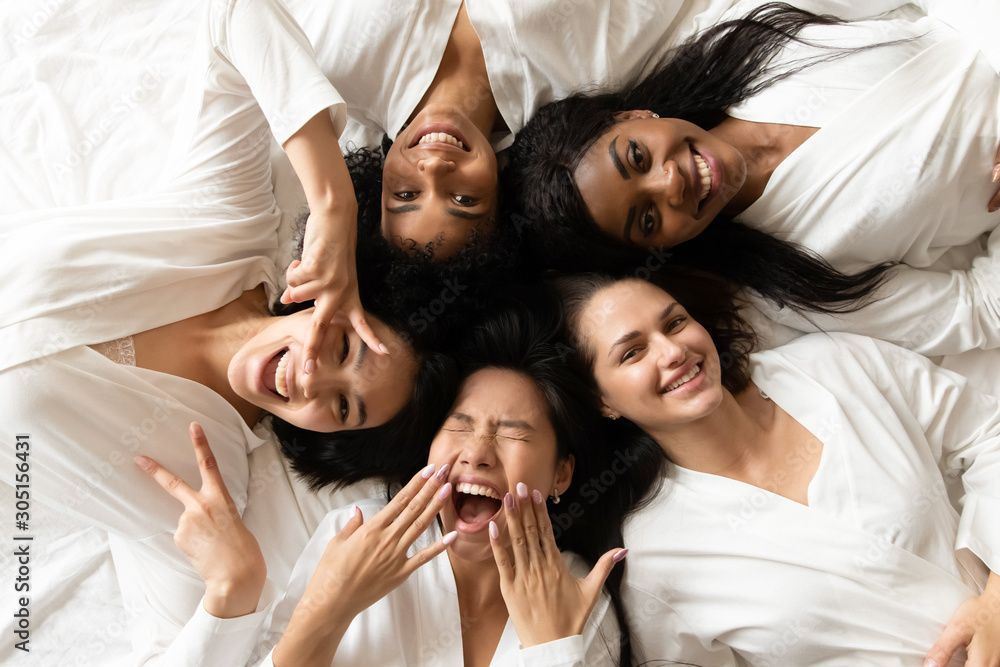 A group of women are laying in a circle on a bed making funny faces.